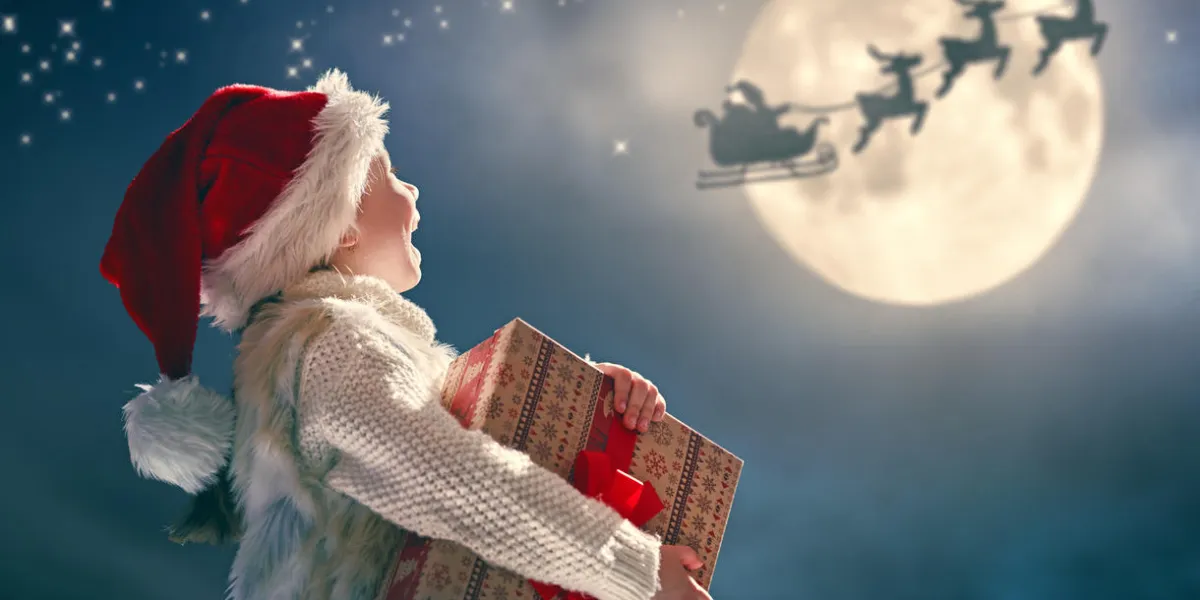 merry christmas cute little child with xmas present santa claus flying in his sleigh against moon sky happy kid enjoy the holiday portrait of girl with gifts on dark background
