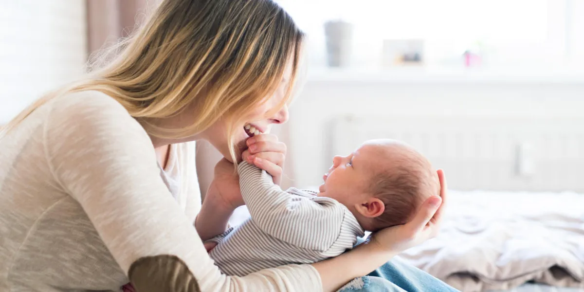 beautiful young mother with her newborn baby son, sitting on bed in her bedroom, caressing him