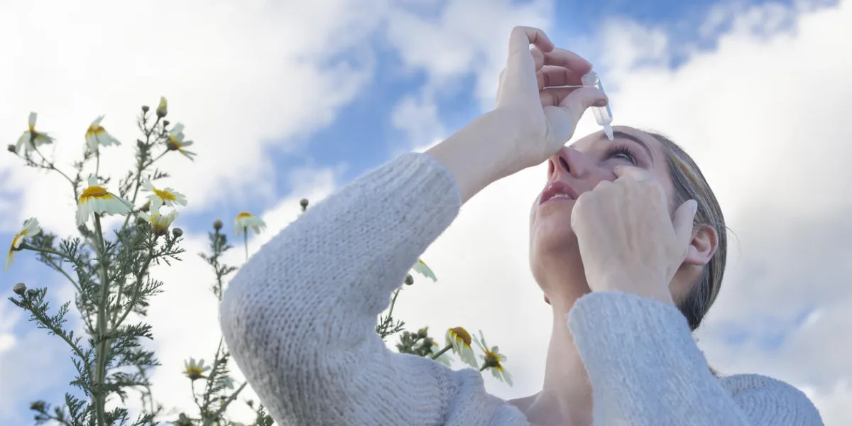 young woman using eyedropper to treat irritated eyes at flowers meadow young woman using eyedropper to treat irritated eyes at flowers meadow