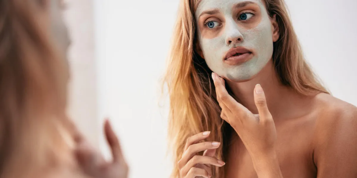 woman looking in the mirror with mask on her face female applying facial cosmetic mask in bathroom woman looking in the mirror with mask on her face female applying facial cosmetic mask in bathroom