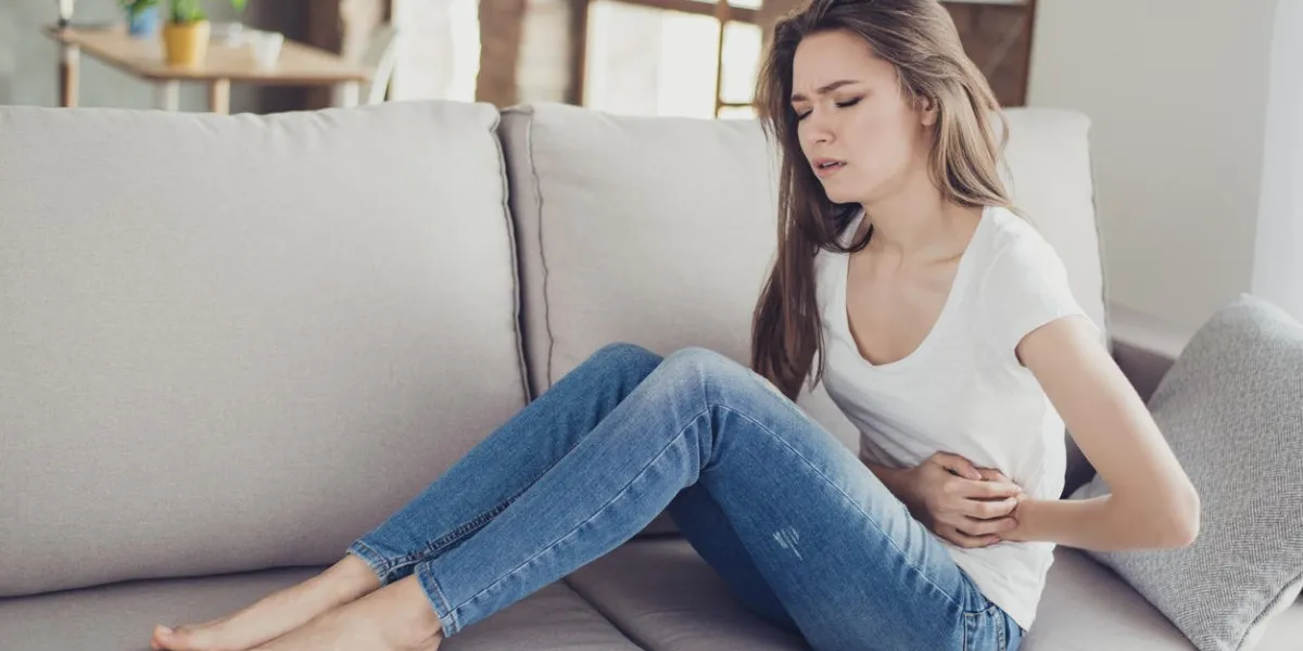 sad beautiful woman sitting on the couch and feeling spasm and symptoms of pms