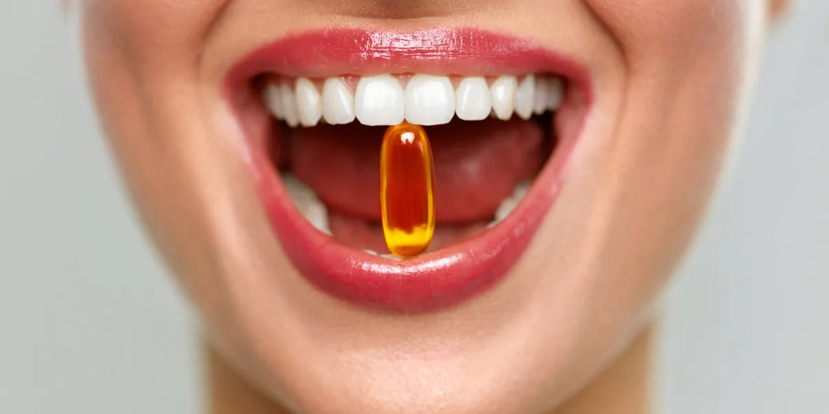vitamins and food supplements close up of beautiful woman opened mouth holding fish oil pill in white teeth smiling girl holding capsule with omega-3 between teeth healthy diet nutrition concept vitamins and food supplements close up of beautiful woman opened mouth holding fish oil pill in white teeth smiling girl holding capsule with omega-3 between teeth healthy diet nutrition concept