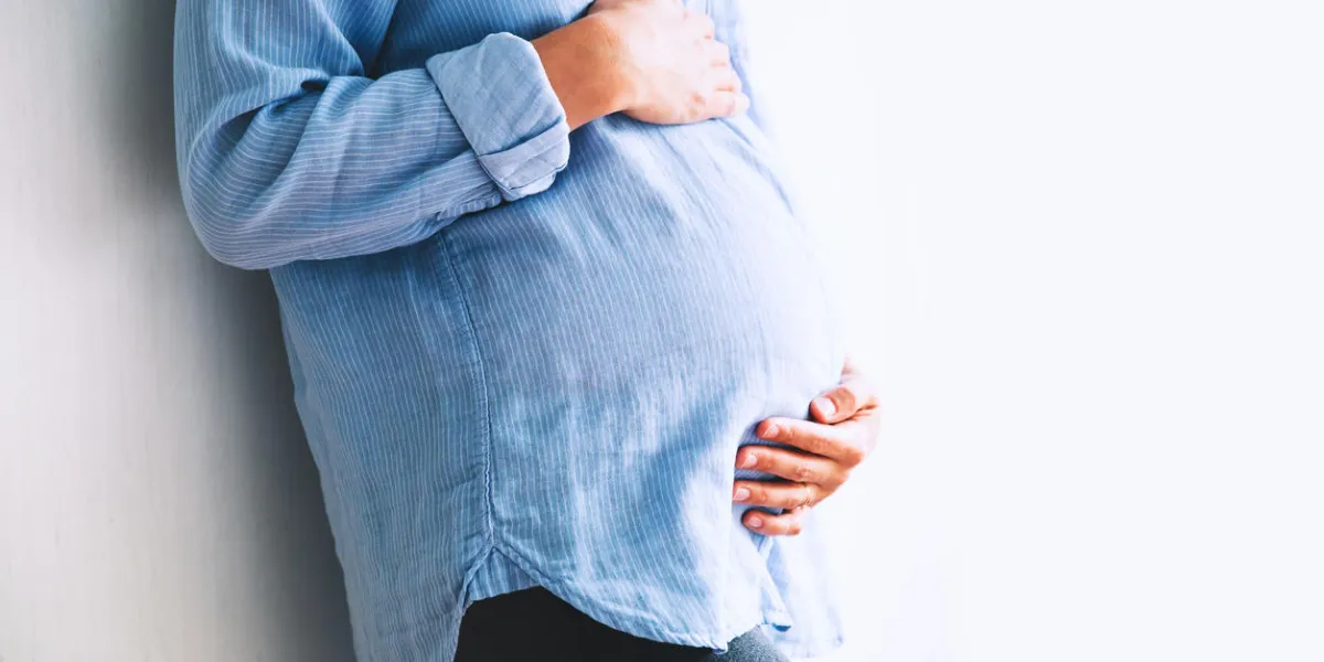 pregnant woman holds hands on belly at home interiors pregnancy, parenthood, preparation and expectation concept close-up, copy space, indoors