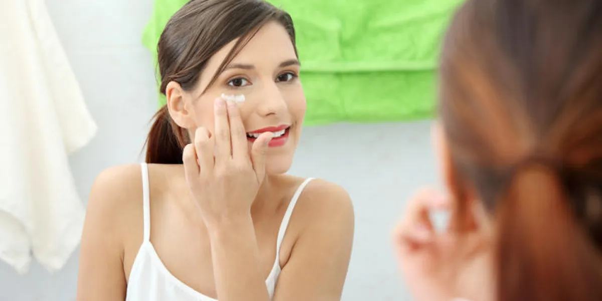 belle jeune femme regardant dans le miroir et appliquer une lotion sur son visage