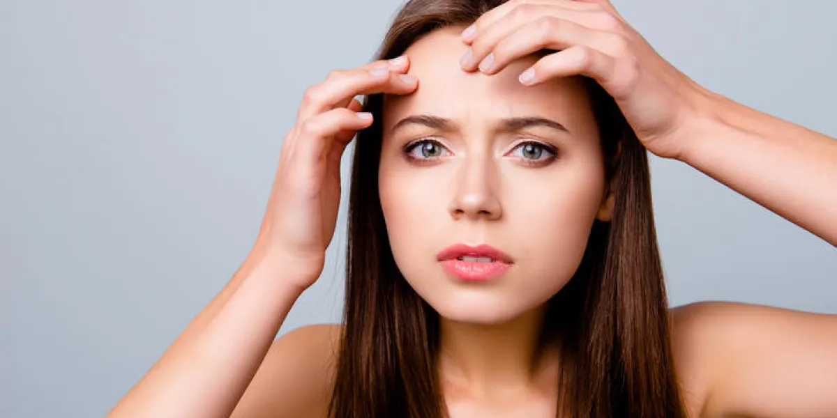 close up portrait of frustrated sad upset beautiful young woman is squeezing out pimples on her forehead, isolated on grey background