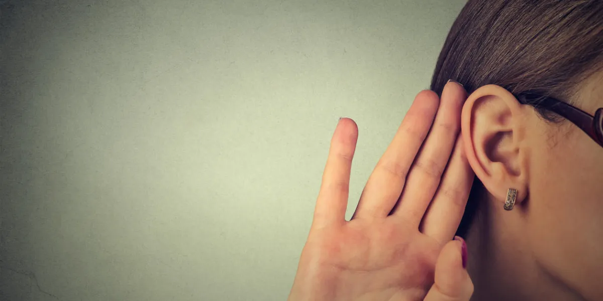 femme tient sa main près de l'oreille et écoute soigneusement isolé sur fond de mur gris