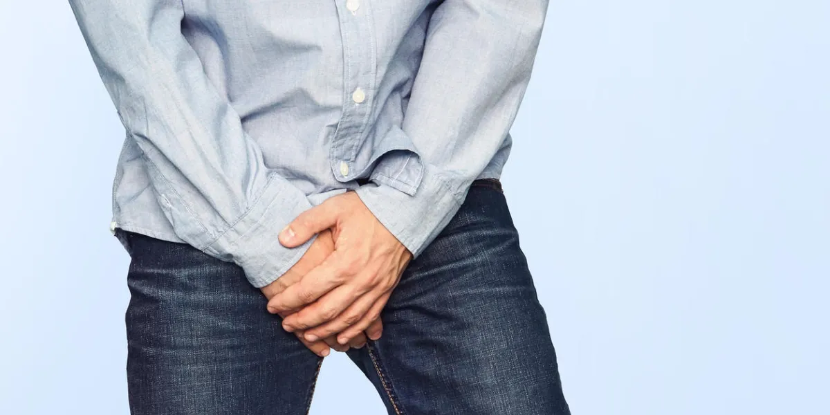 close up of a man with hands holding his crotch on a light blue background urinary incontinence men's health the pain from the blow in groin close up of a man with hands holding his crotch on a light blue background urinary incontinence men's health the pain from the blow in groin