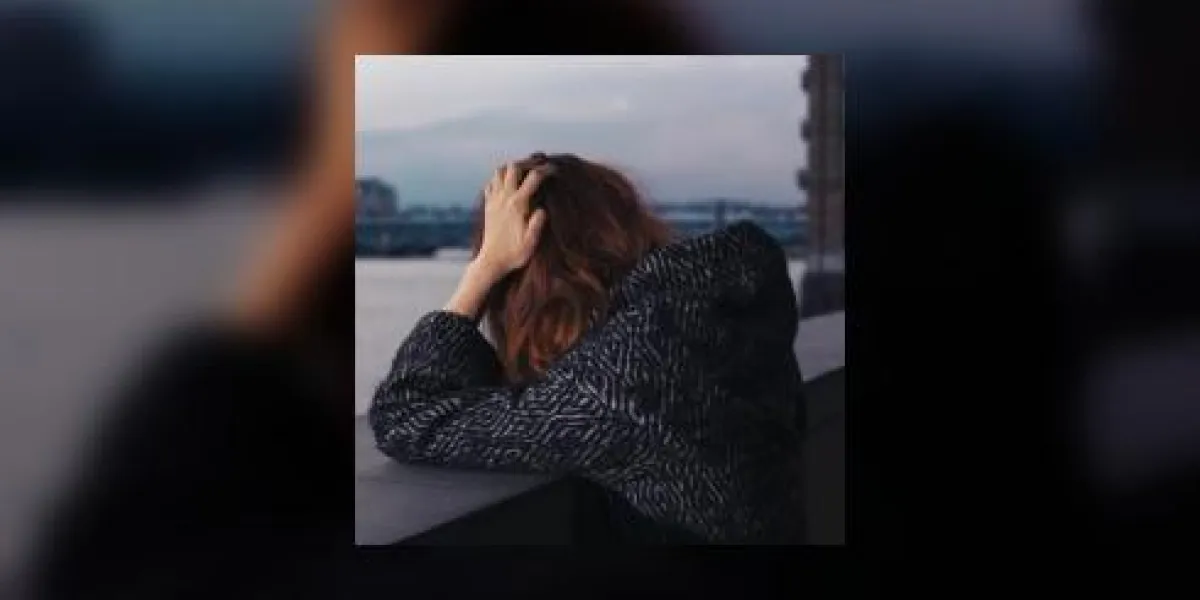 une femme triste est debout près d'une rivière dans la ville et se tient la tête