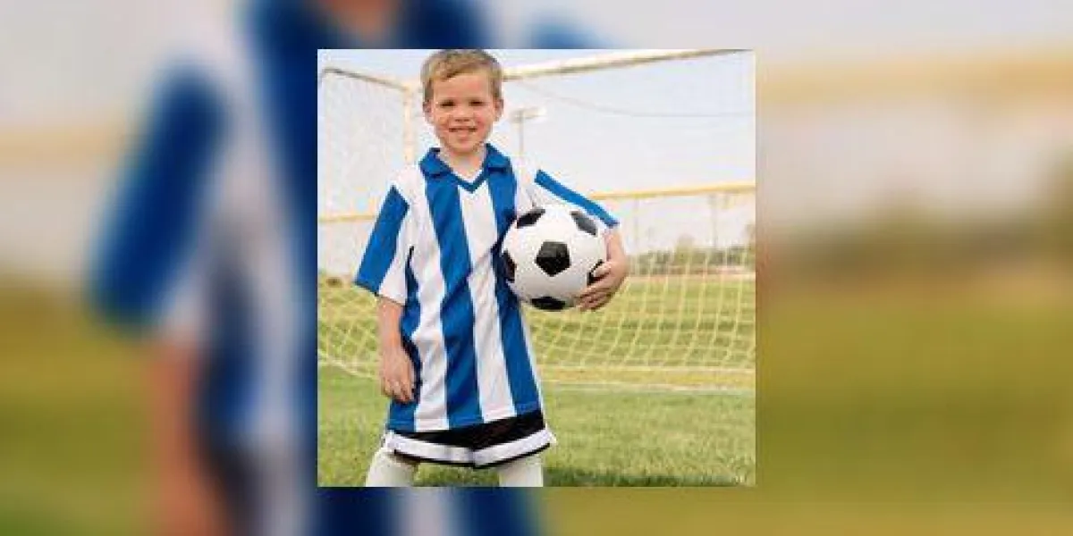 garçon en uniforme de football tenant le ballon de soccer par but