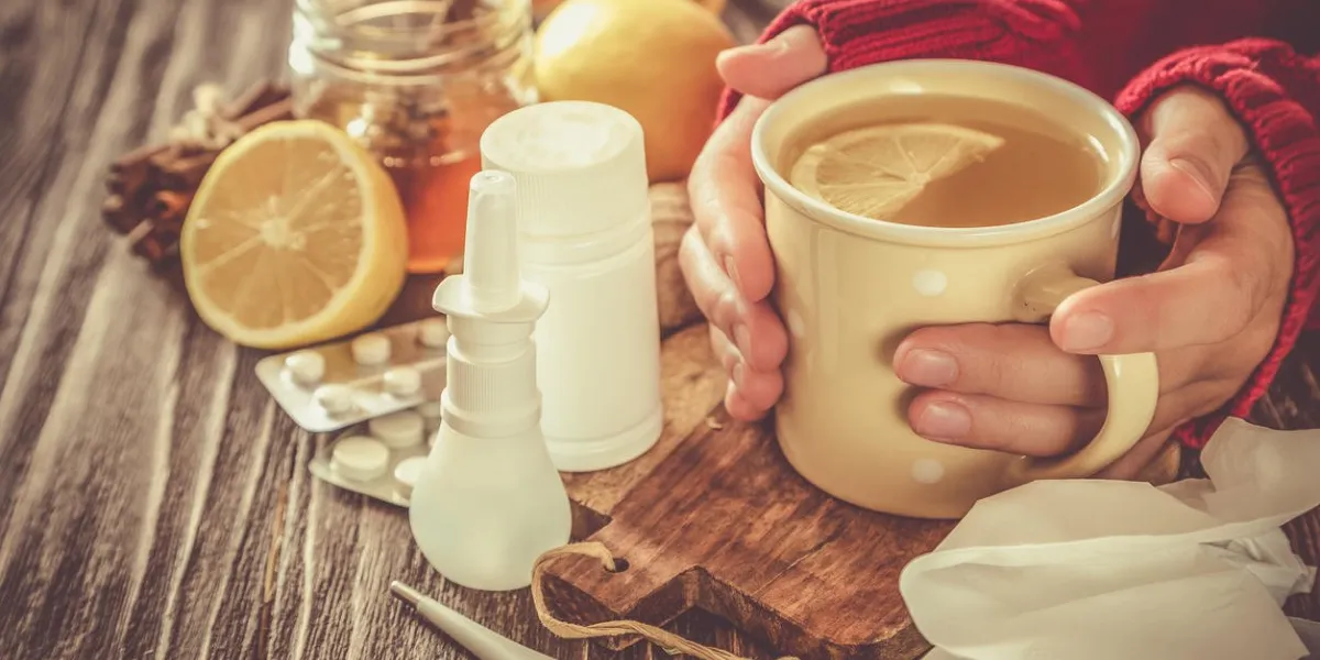 medical care concept - hands holding cup with ginger honey and lemon tea with drugs, pills and spray on wood background medical care concept - hands holding cup with ginger honey and lemon tea with drugs, pills and spray on wood background