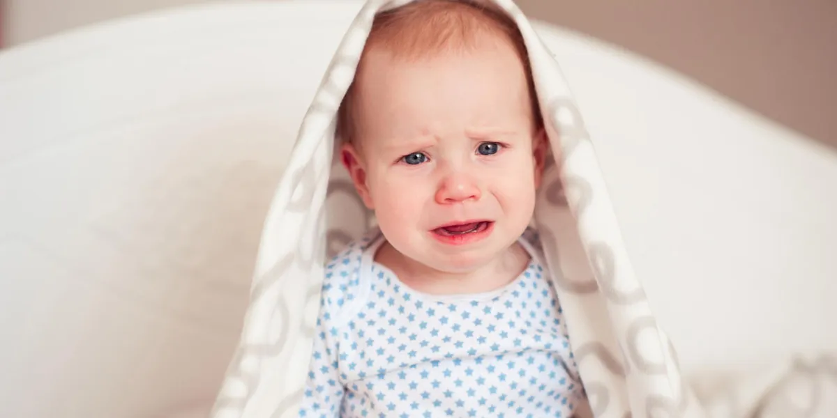crying baby boy 8-9 months sitting in bed looking at camera sadness childhood