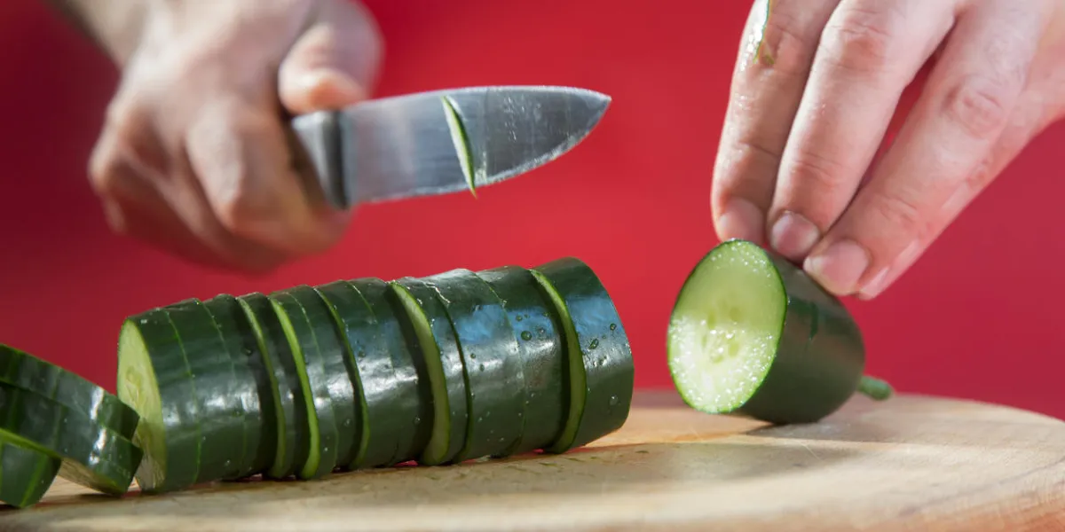 gros plan d'un homme hacher le concombre avec un couteau de cuisine sur une planche à découper