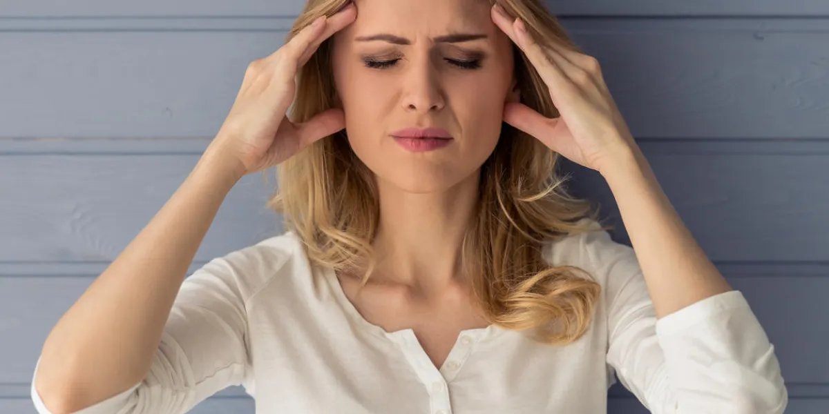 portrait of beautiful tired young woman having headache, massaging her temples, against gray wall portrait of beautiful tired young woman having headache, massaging her temples, against gray wall