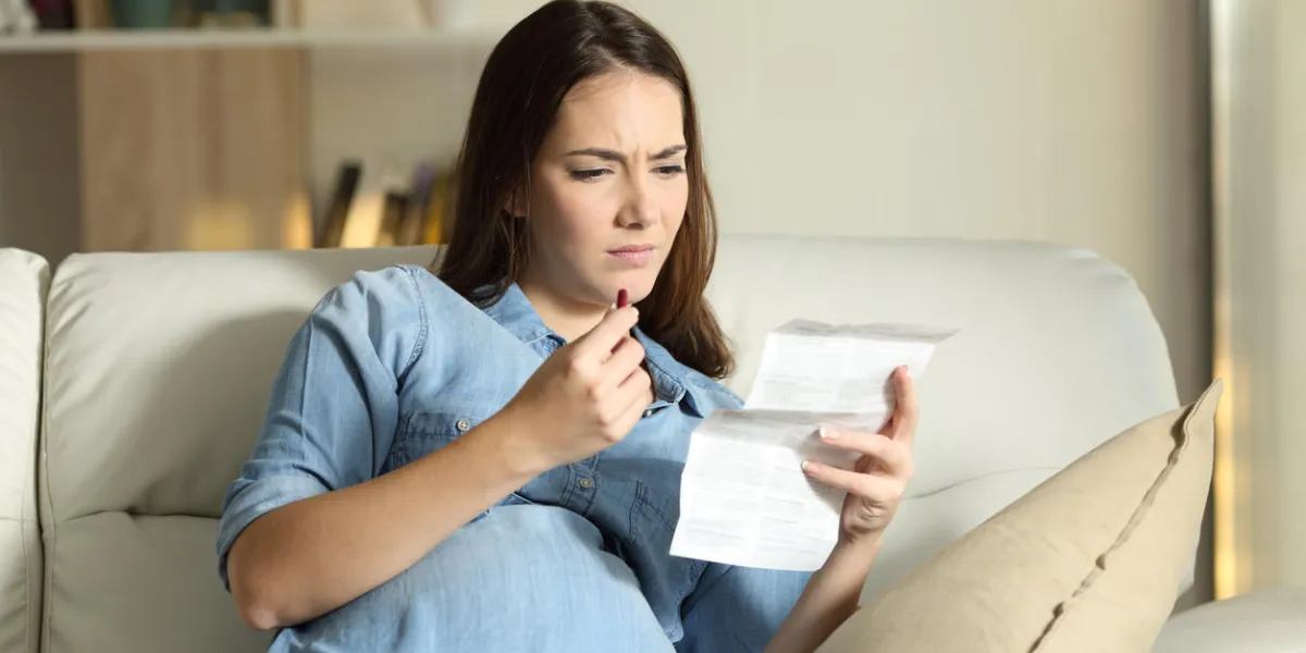 confused pregnant woman reading a leaflet before take a pill sitting on a couch in the living room at home confused pregnant woman reading a leaflet before take a pill sitting on a couch in the living room at home