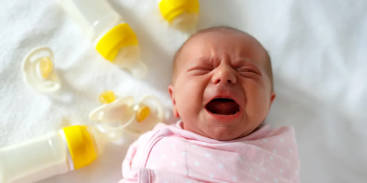 crying newborn baby girl with nursing bottles formula drink for babies new born child, little girl laying in bed family, new life, childhood, beginning, bottle-feeding concept