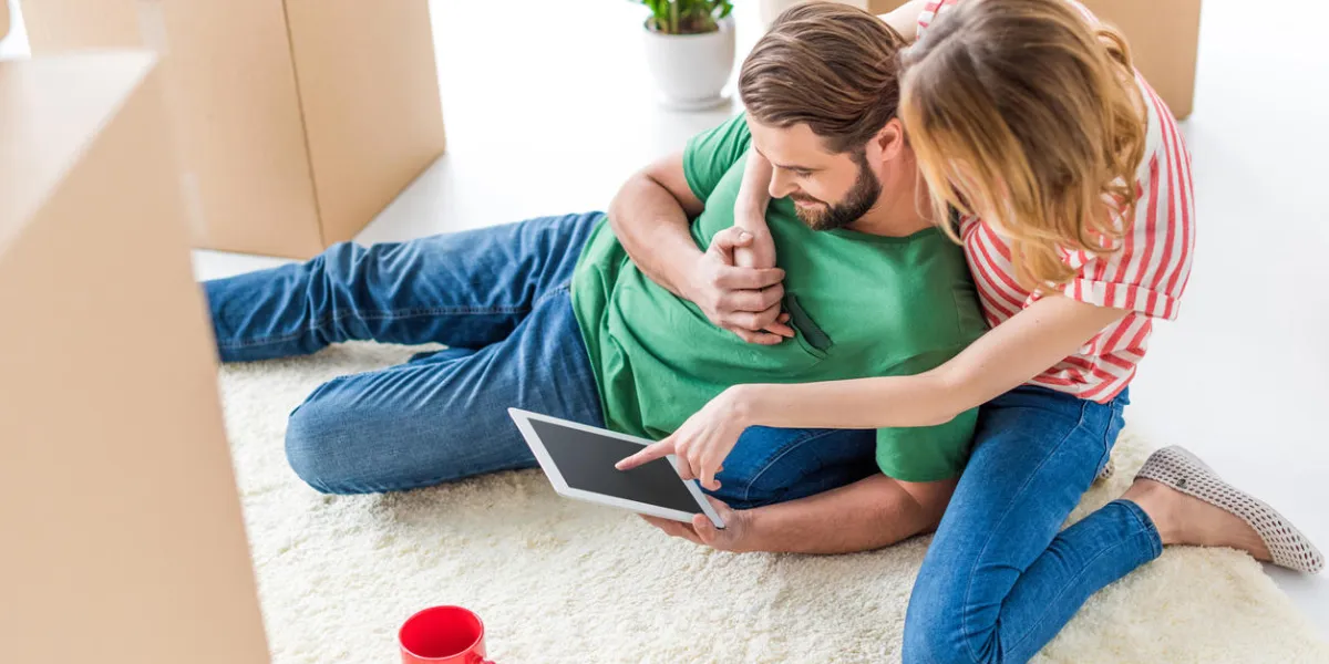 couple sitting on carpet, using digital tablet and drinking tea among cardboard boxes couple sitting on carpet, using digital tablet and drinking tea among cardboard boxes