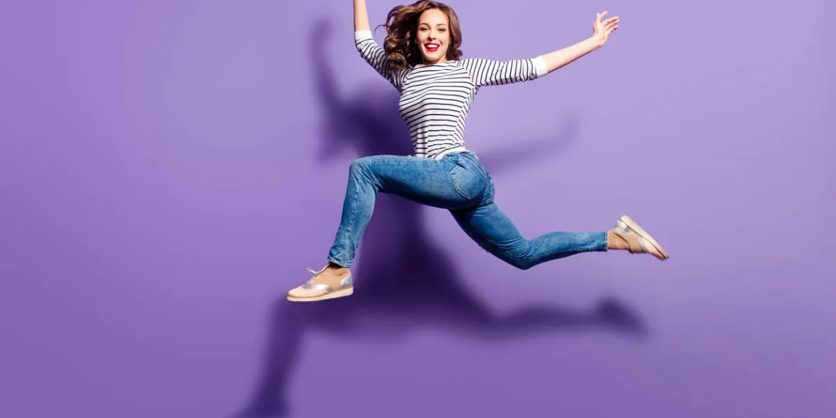 portrait of crazy foolish girl jumping over in the air looking at camera having good stretching isolated on violet background, people life energy lifestyle concept