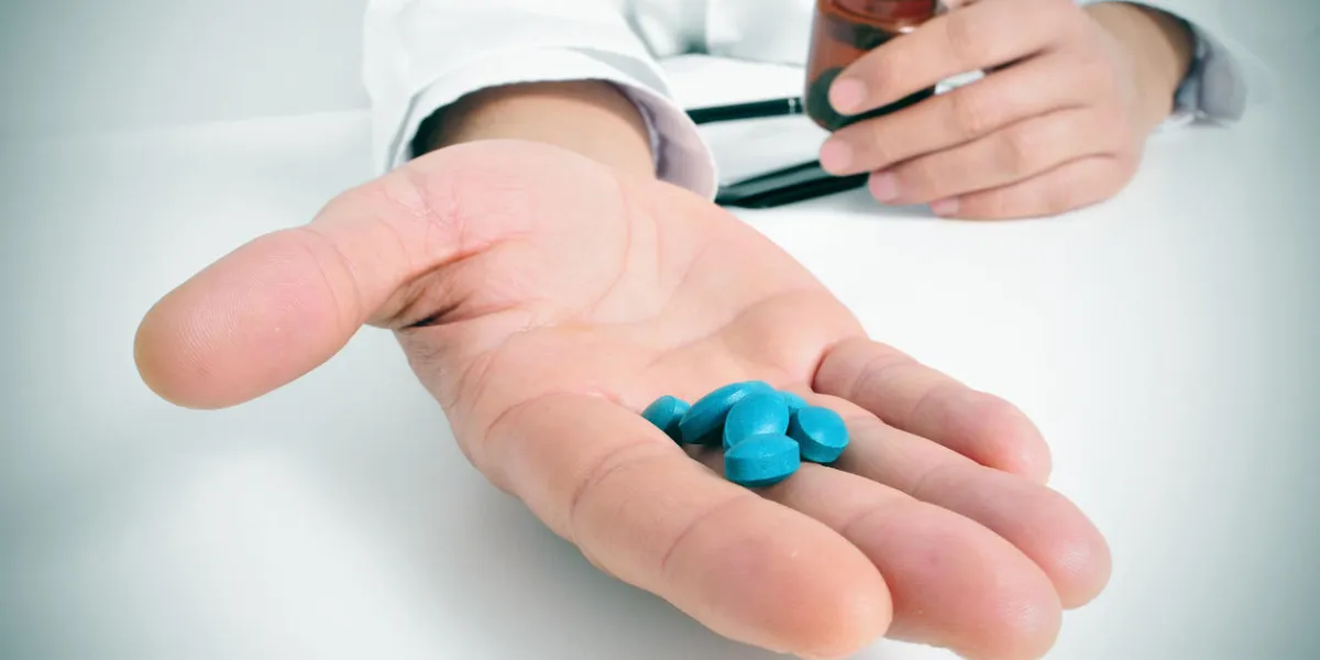 a doctor in a consulting room with a pile of blue pills in his hand a doctor in a consulting room with a pile of blue pills in his hand