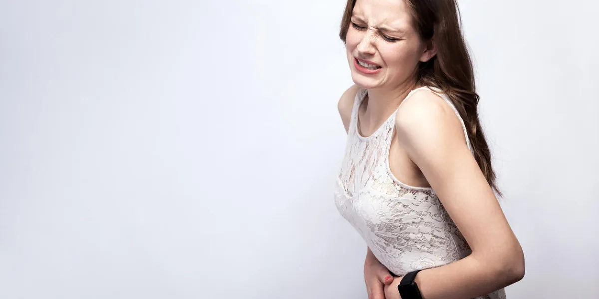 portrait of beautiful woman with freckles and white dress and smart watch with stomach pain on silver gray background healthcare and medicine concept