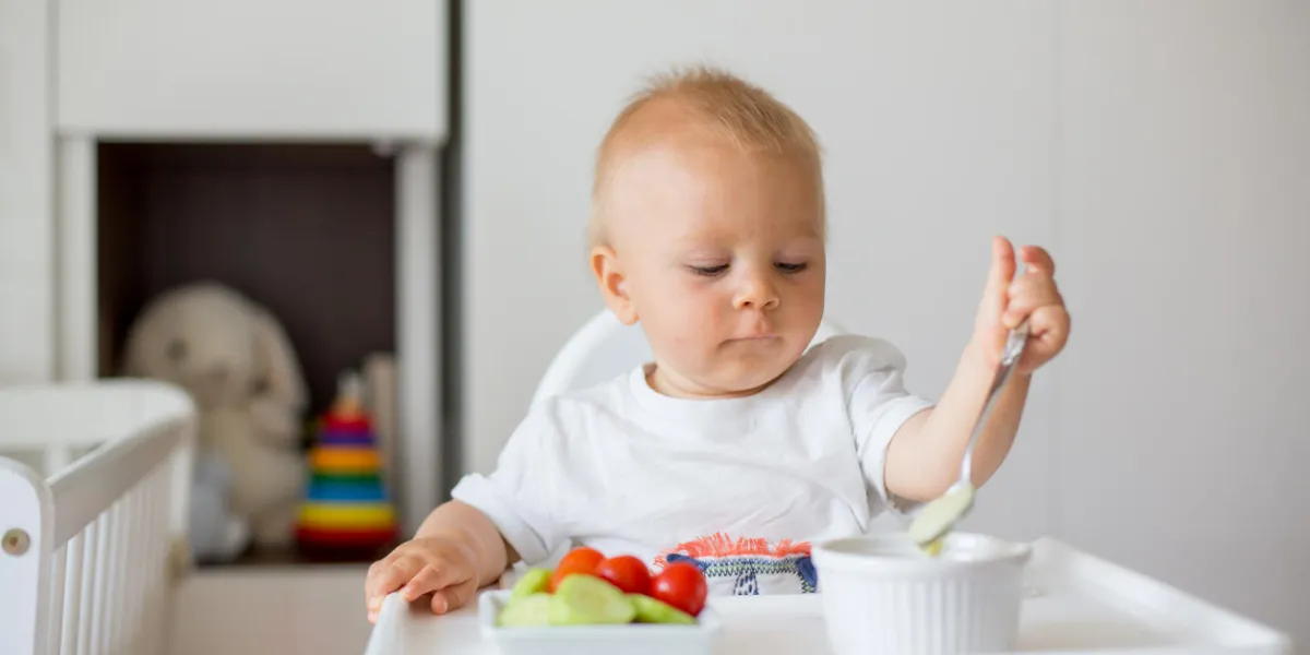 sweet baby child, boy, eating mashed food and fresh vegetables, sitting in high baby chair in kids room