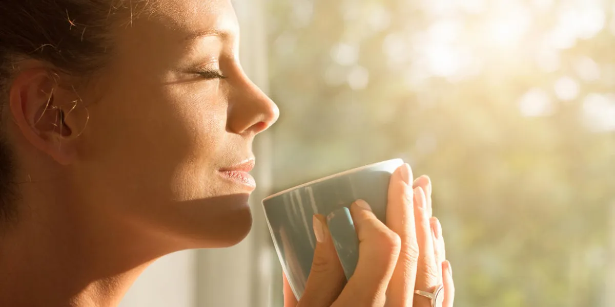 pretty young woman enjoying first morning coffee on sunshine by window