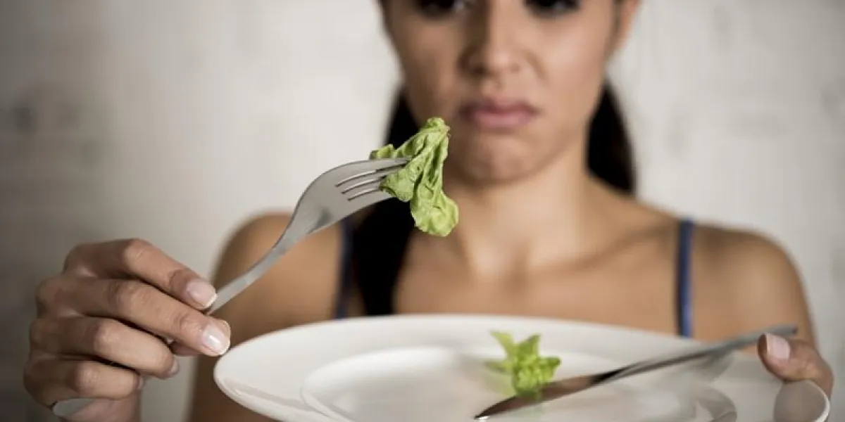 young woman or teen girl holding dish with ridiculous little lettuce as her food symbol of crazy diet in nutrition disorder concept anorexia and bulimia and refusing to eat in diet calories obsession