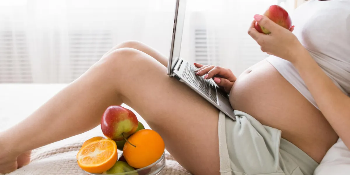 pregnant woman eats apple while chatting in laptop work and relax combining, fresh fruits and healthcare concept of special mother-to-be period pregnant woman eats apple while chatting in laptop work and relax combining, fresh fruits and healthcare concept of special mother-to-be period