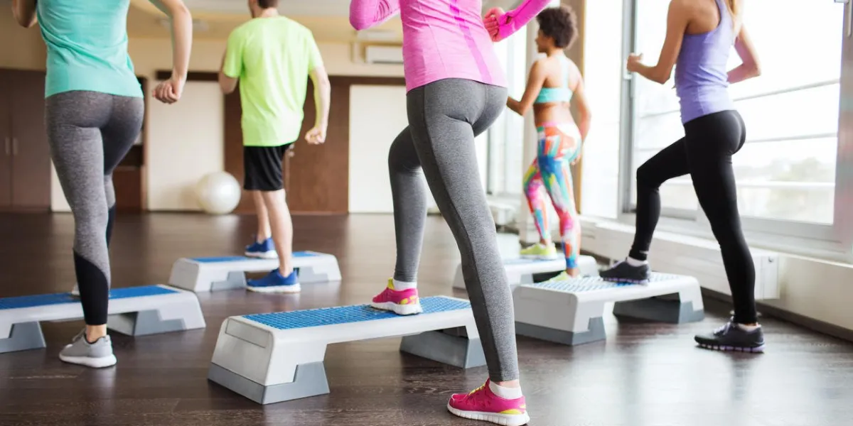 fitness, sport, training, aerobics and people concept - close up of people working out with steppers in gym from back