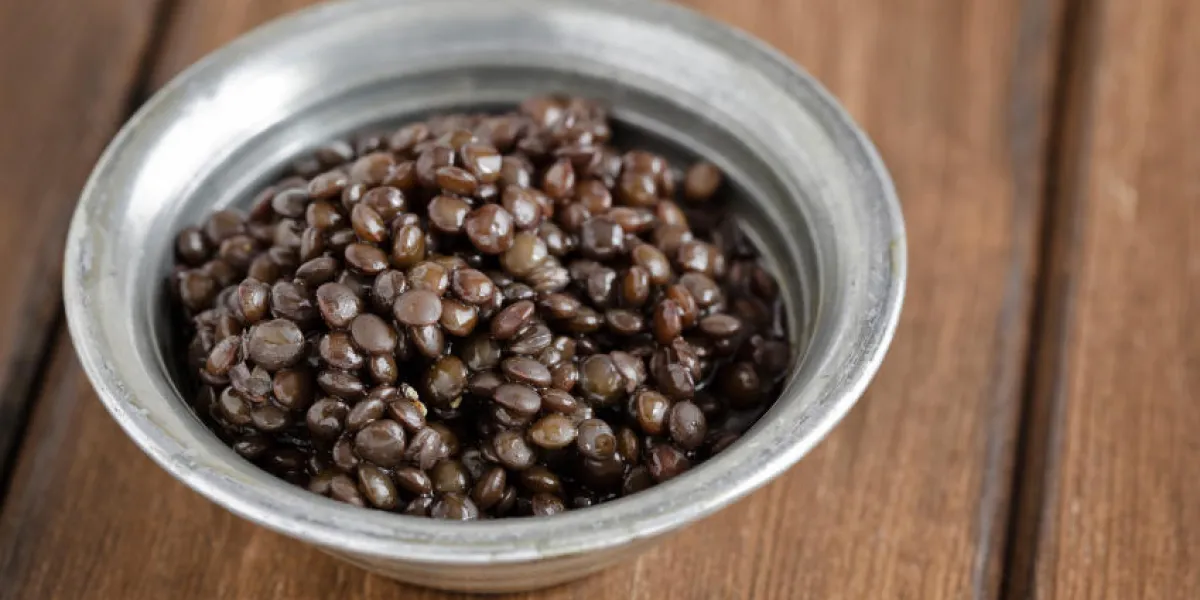 petit bol en argent avec des lentilles noires cuites sur une planche de bois petit bol en argent avec des lentilles noires cuites sur une planche de bois