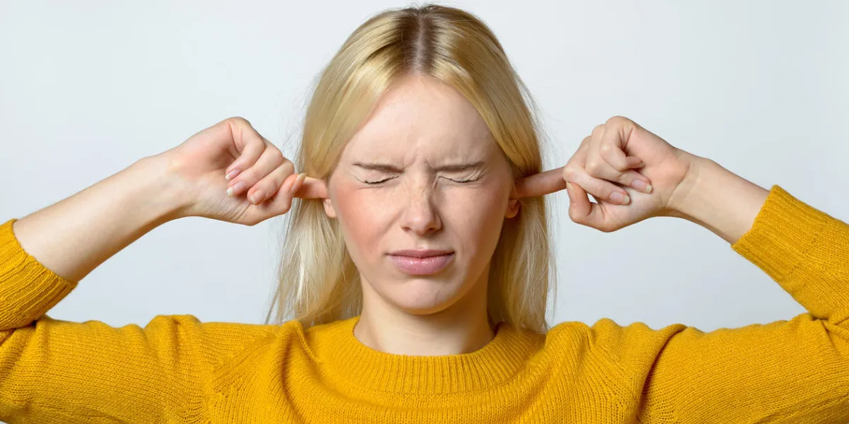 close up disgusted young woman covering her ears with fingers, with eyes closed, against gray background