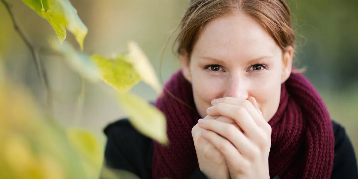 une jeune femme réchauffe ses mains de son propre souffle alors qu'elle regarde la caméra photographiée dans un parc à l'automne ou à l'automne