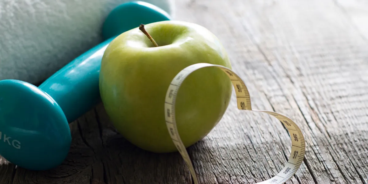love fitness and diet concept with heart measuring tape apple and dumbbell closeup