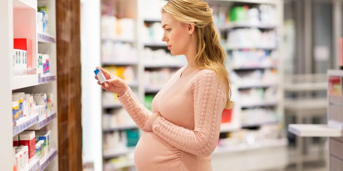 pregnancy, medicine, people, healthcare and expectation concept - happy pregnant woman with medication at pharmacy
