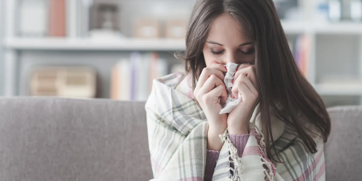 sick young woman at home on the sofa with a cold, she is covering with a blanket and blowing her nose
