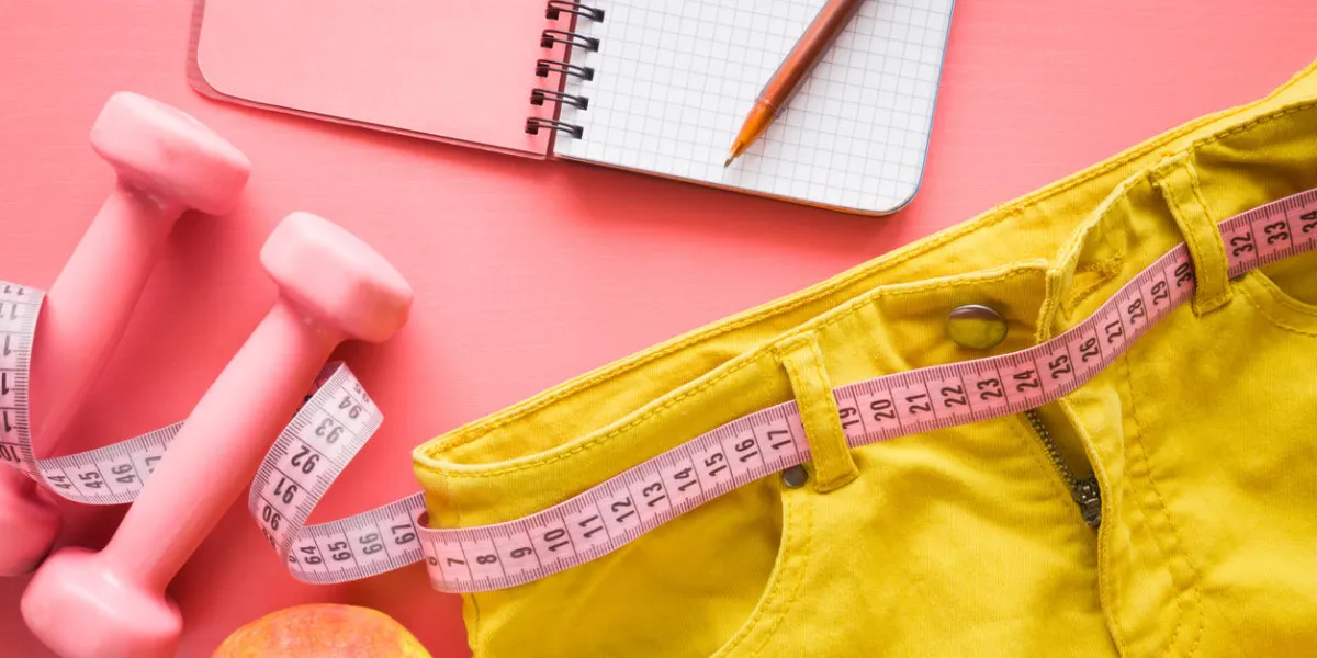 measure tape with yellow jeans, dumbbells, apple, notebook on the pastel pink background women diet before summer season healthy lifestyle, body slimming, weight loss concept cares about body measure tape with yellow jeans, dumbbells, apple, notebook on the pastel pink background women diet before summer season healthy lifestyle, body slimming, weight loss concept cares about body
