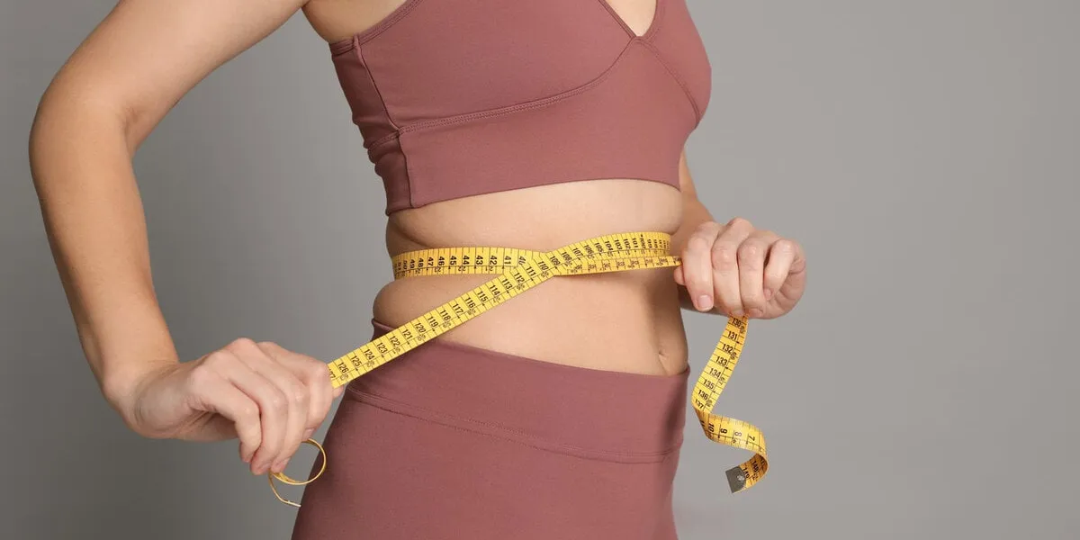 woman measuring waist with tape on grey background, closeup