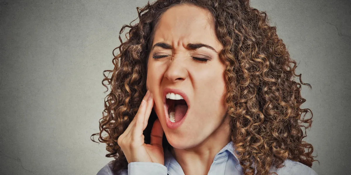 closeup portrait young woman with sensitive tooth ache crown problem about to cry from pain touching outside mouth with hand isolated grey wall background negative emotion facial expression feeling