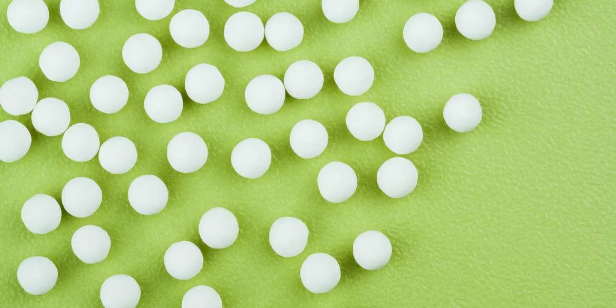 homeopathic pills background - overhead horizontal view of homeopathic medicinal pills (made from an inert substance - sugar lactose) spillage on a green tabletop