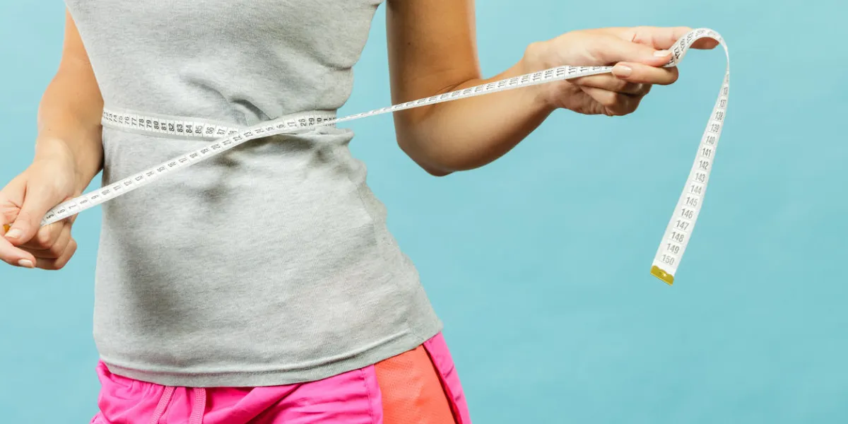 weight loss, slim body, healthy lifestyle concept fit fitness girl measuring her waistline with measure tape on blue weight loss, slim body, healthy lifestyle concept fit fitness girl measuring her waistline with measure tape on blue