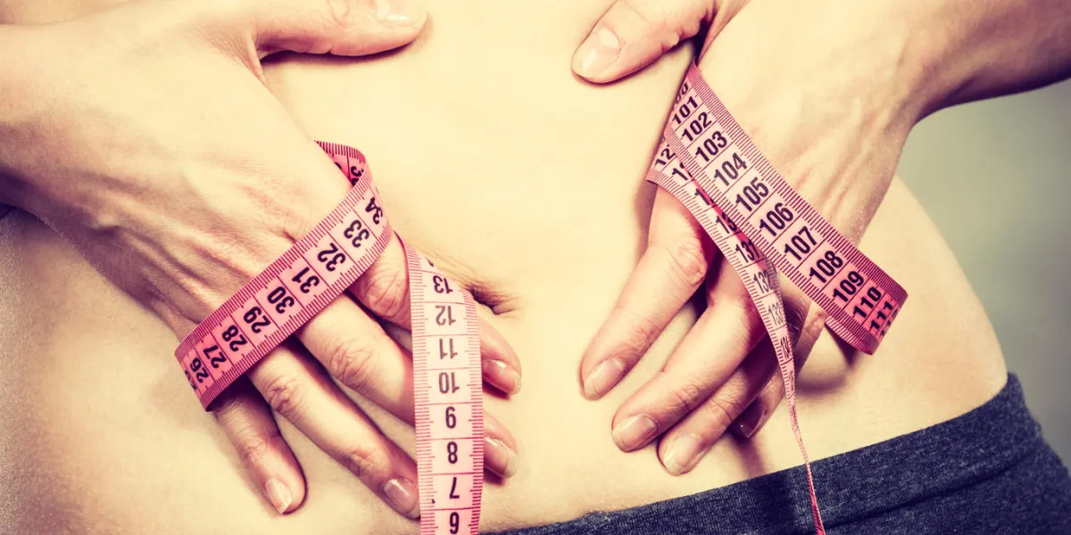 getting rid of belly fat, diet, weight loss or gain concept woman touching stomach holding measuring tape