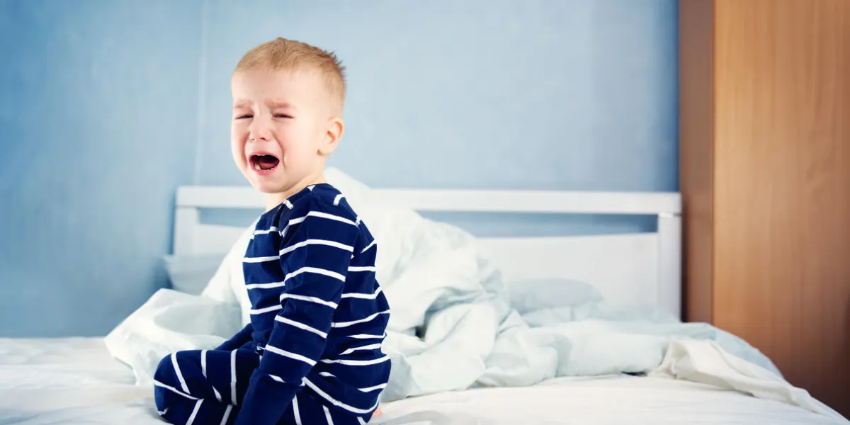 sleepy boy sitting in bed and crying tired child in bedroom