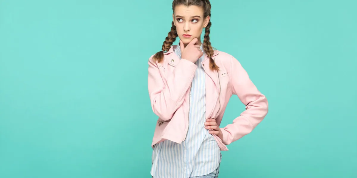 confused thinking portrait of beautiful cute girl standing with makeup and brown pigtail hairstyle in striped light blue shirt pink jacket indoor, studio shot isolated on blue or green background confused thinking portrait of beautiful cute girl standing with makeup and brown pigtail hairstyle in striped light blue shirt pink jacket indoor, studio shot isolated on blue or green background