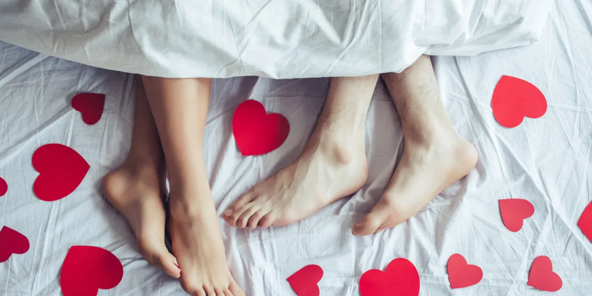 cropped image of young couple is lying on bed close up of male and female feet loving couple is lying on bed under blanket covered by small red paper hearts saint valentines day cropped image of young couple is lying on bed close up of male and female feet loving couple is lying on bed under blanket covered by small red paper hearts saint valentines day
