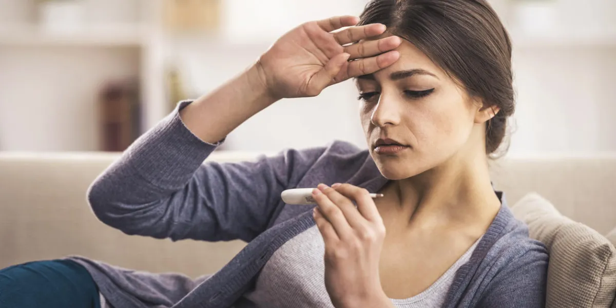 young woman is looking at the thermometer she has fever