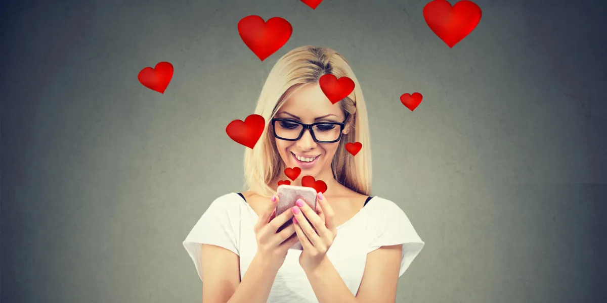 beautiful woman sending love text message on mobile phone with red hearts flying away from screen isolated on gray background
