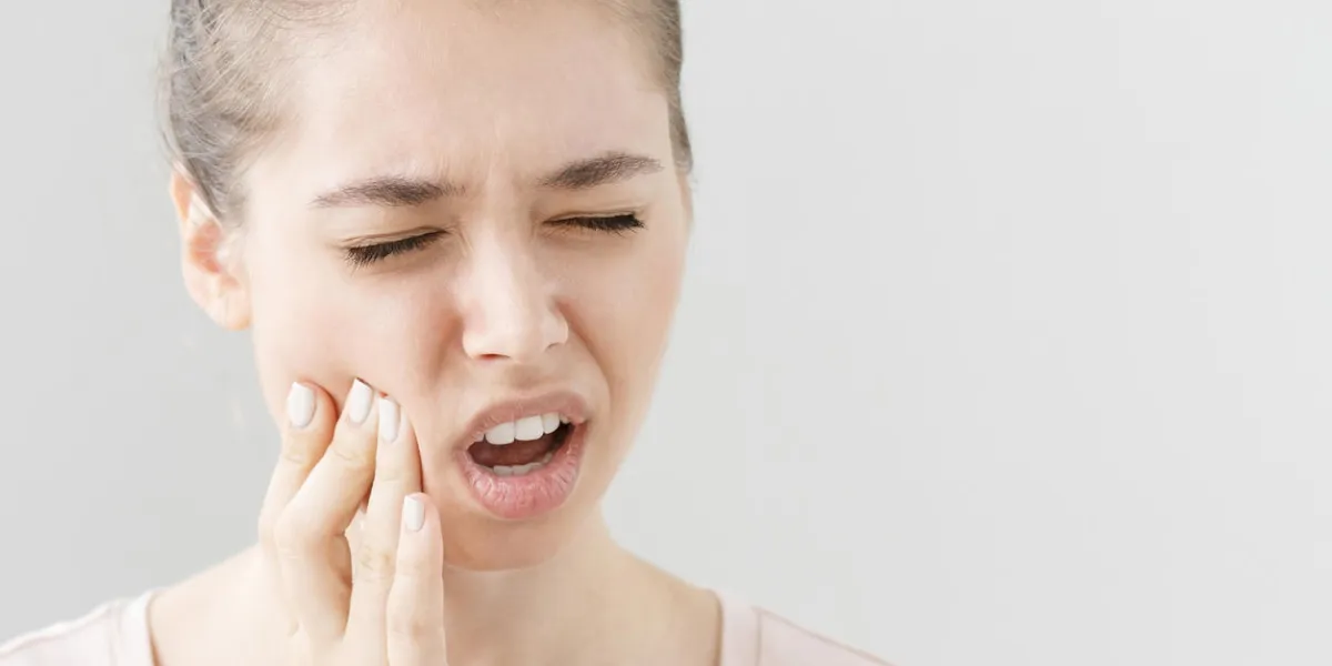 close headshot of young european female isolated on grey background suffering from severe toothache, feeling pain so strong that she is pressing fingers to cheek to calm it down, looking desperate close headshot of young european female isolated on grey background suffering from severe toothache, feeling pain so strong that she is pressing fingers to cheek to calm it down, looking desperate