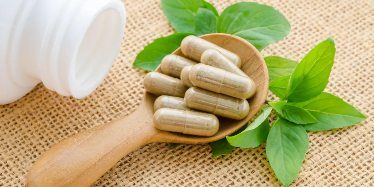 capsule d'herbe renversant d'une bouteille blanche dans la cuillère en bois avec feuille verte sur fond de sac capsule d'herbe renversant d'une bouteille blanche dans la cuillère en bois avec feuille verte sur fond de sac
