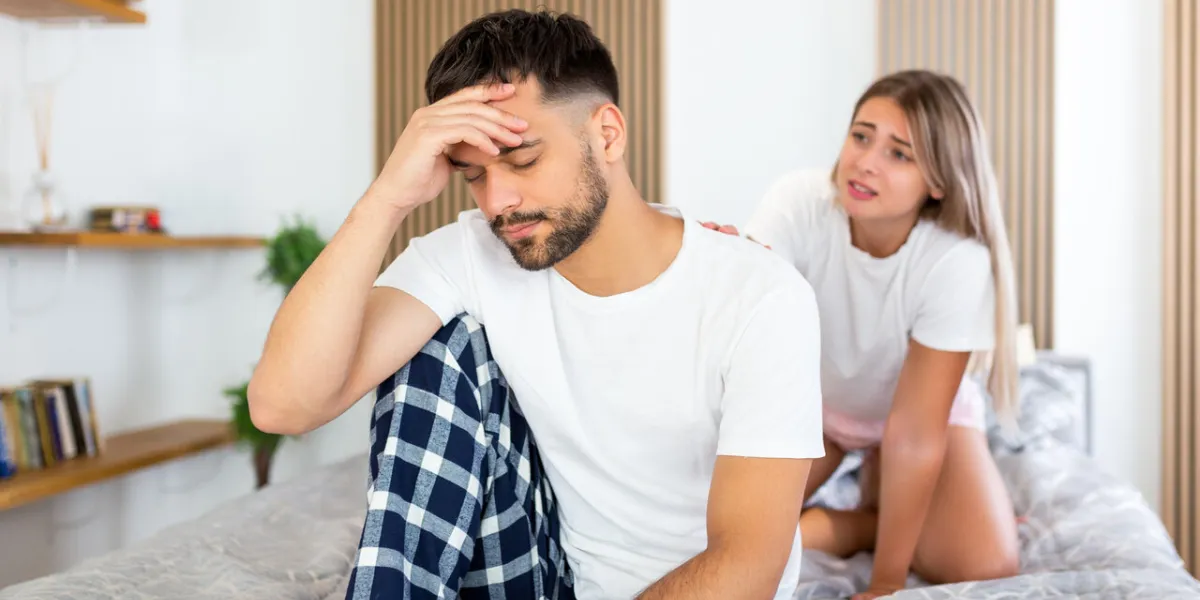 young sad man sitting on bed after quarrel with wife hotel, travel, relationships, and sexual problems concept - upset man sitting on the bed with woman on the back young sad man sitting on bed after quarrel with wife hotel, travel, relationships, and sexual problems concept - upset man sitting on the bed with woman on the back