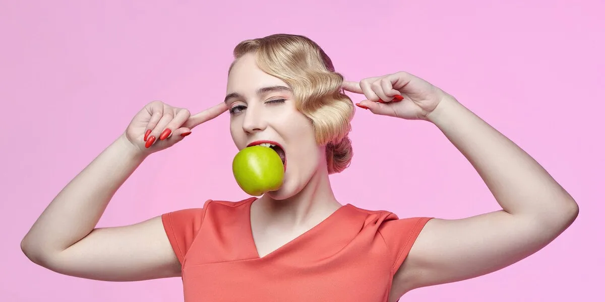 attractive young blonde with a retro hairstyle holds a green apple in her teeth attractive young blonde with a retro hairstyle holds a green apple in her teeth