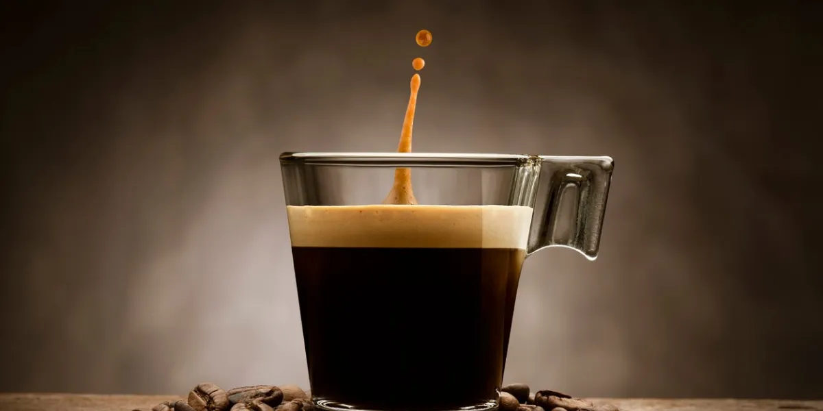 black coffee in glass cup with coffee beans and jumping drop, on wooden table
